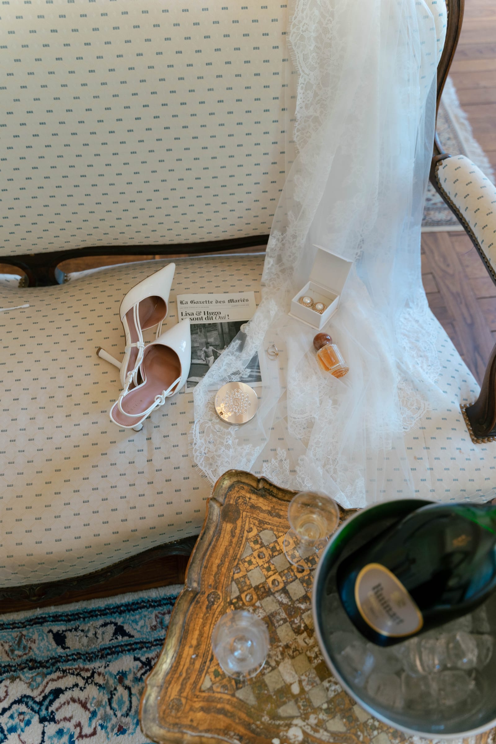 Les accessoires de la mariée sur une banquette : escarpins blancs, boucles d’oreilles, parfum, gazette du mariage et champagne au frais.