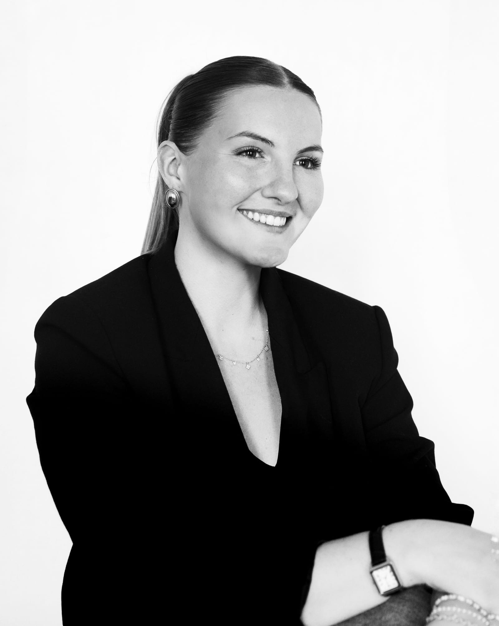 Portrait en noir et blanc d’Anna Aguerre, souriante, cheveux tirés en queue de cheval, en blazer noir.